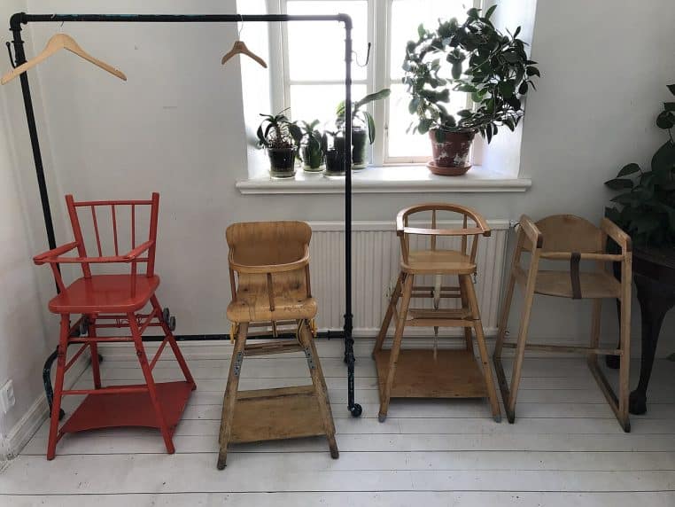 Rang de chaises hautes en bois, rouges et naturelles, alignées contre un mur blanc près d’une fenêtre lumineuse dans un café suédois.
