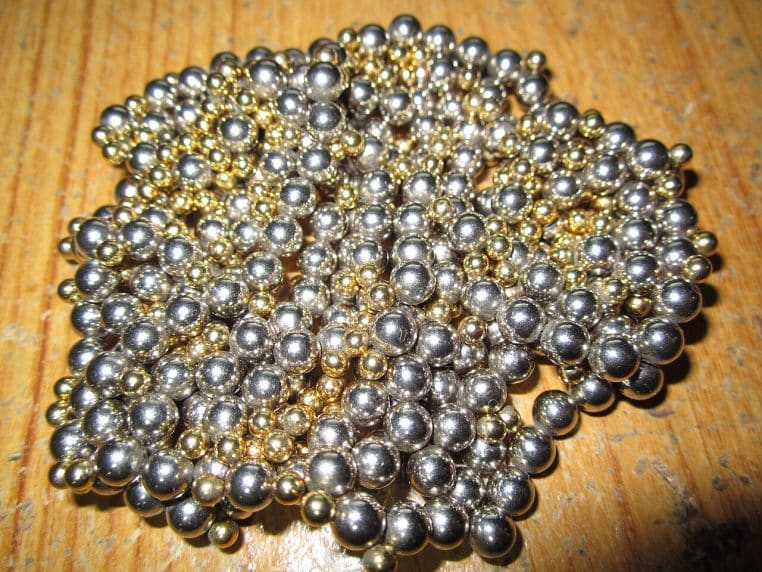 Piles d’aimants au néodyme brillants, alignés en colonnes sur un fond neutre, éclairage studio.