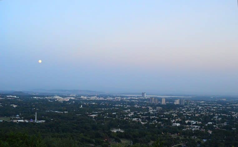 Super Lune lumineuse au-dessus d’Islamabad, vue large avec collines sombres et ville éclairée en premier plan, composition horizontale