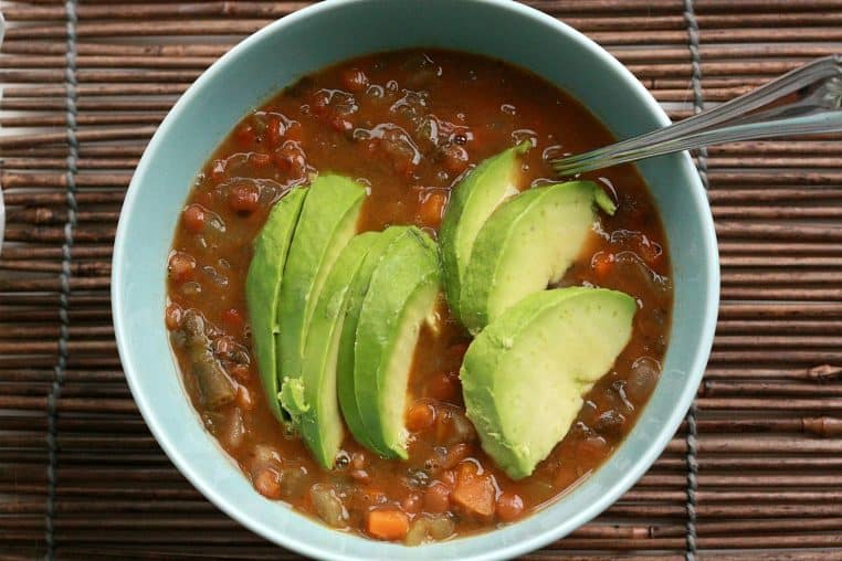 Bol de soupe de lentilles aux légumes garni d’avocat.