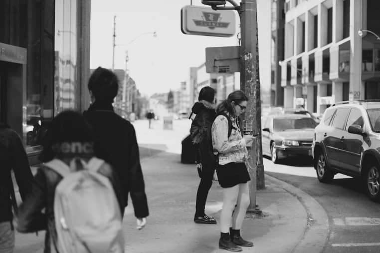 Femme vérifiant son téléphone en ville, métaphore des démarches bancaires en ligne.