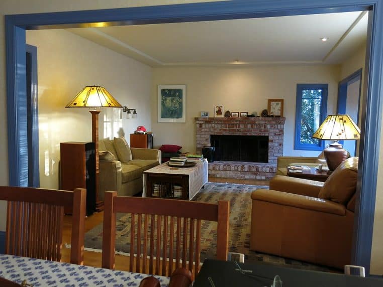 Salon familial avec canapé, table basse, lampe de lecture et cheminée en briques.