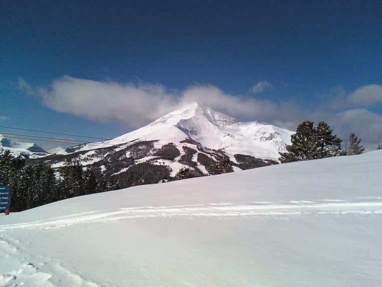 Sommet enneigé de Lone Peak à Big Sky sous ciel bleu, pistes forestières au premier plan, emblème des grands espaces du Montana en hiver.