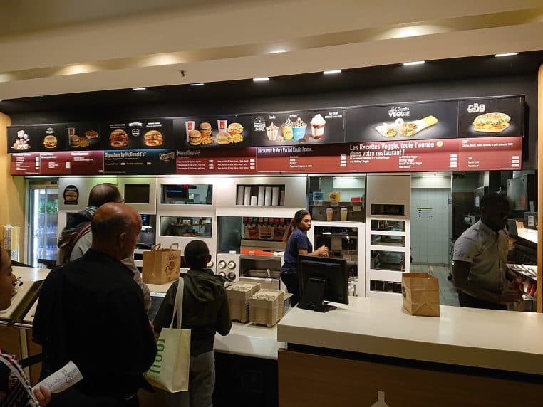 Intérieur d’un McDonald’s parisien avec bornes et écrans de menu.