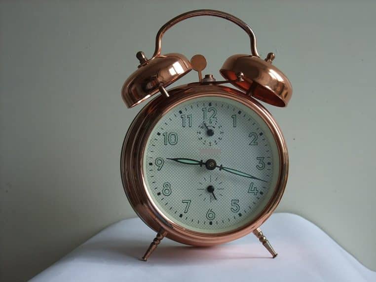 Réveil noir ancien sur table en bois, cadran lisible, profondeur de champ réduite pour une scène chaleureuse.