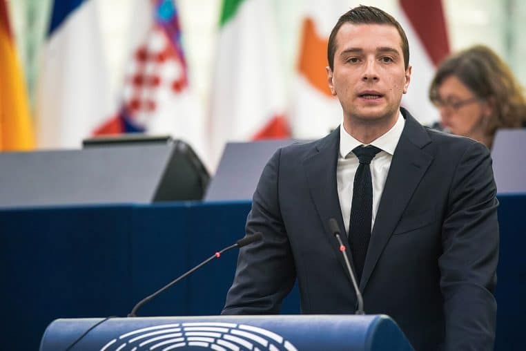 Jordan Bardella photographié en séance plénière, hémicycle du Parlement européen en arrière-plan, ambiance institutionnelle.