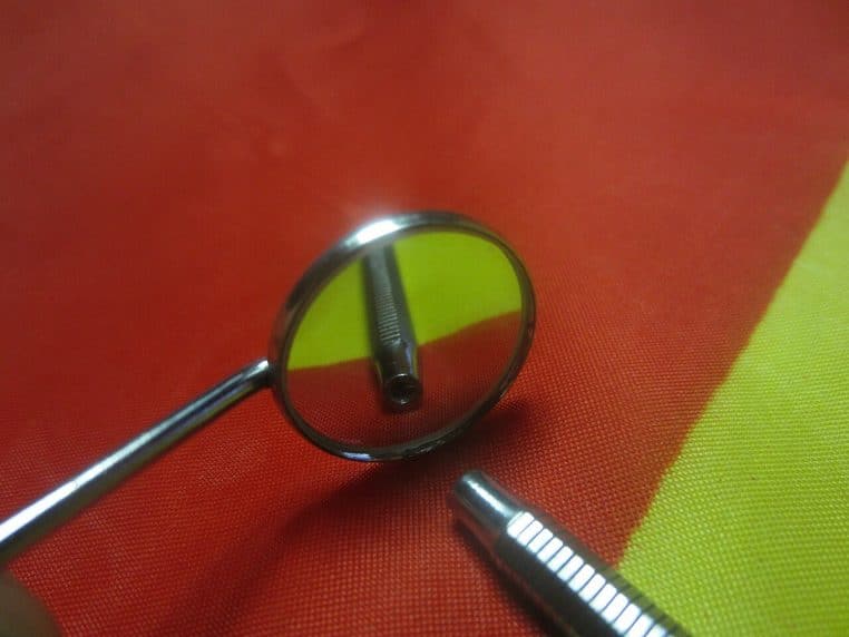 Miroir dentaire en acier posé sur fond neutre.