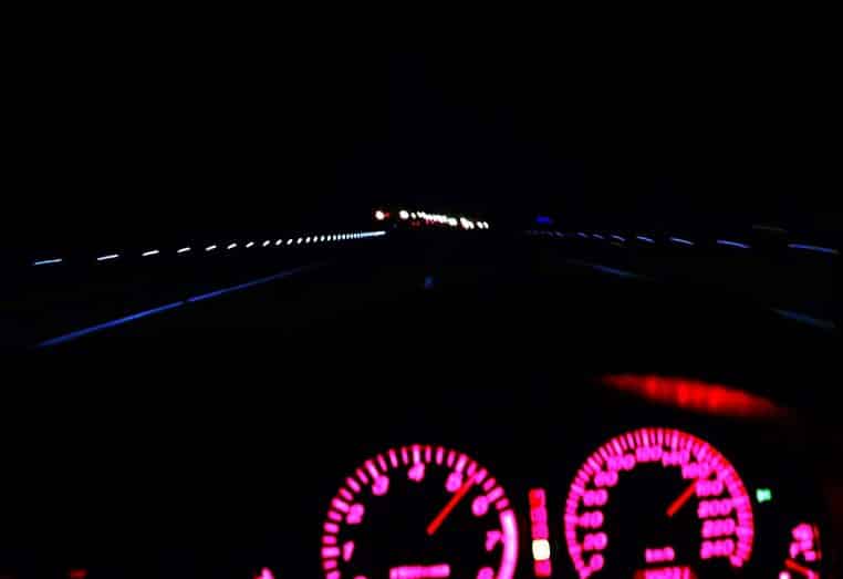 Autoroute malaisienne de nuit avec file de voitures et catadioptres visibles.