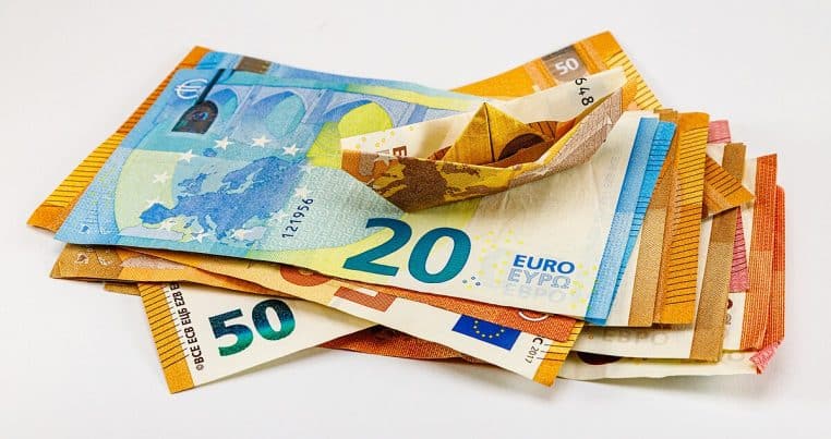 Billets en euros étalés sur une table, dont l’un plié en bateau en papier, cadrage horizontal.