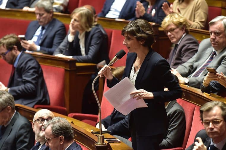 Députée s’exprimant dans l’hémicycle, pupitre et bancs visibles.