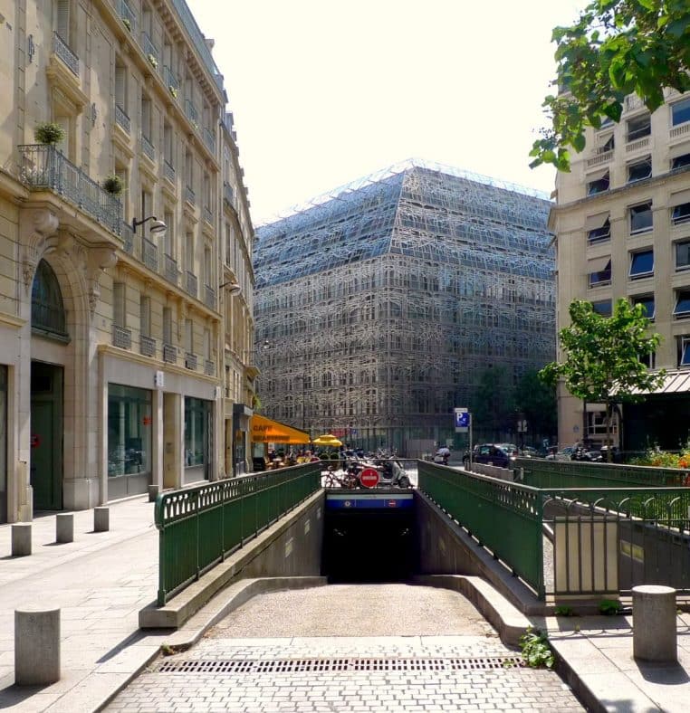 Rampe d’entrée d’un parking souterrain au centre de Paris, bâtiments haussmanniens et immeuble moderne au second plan.