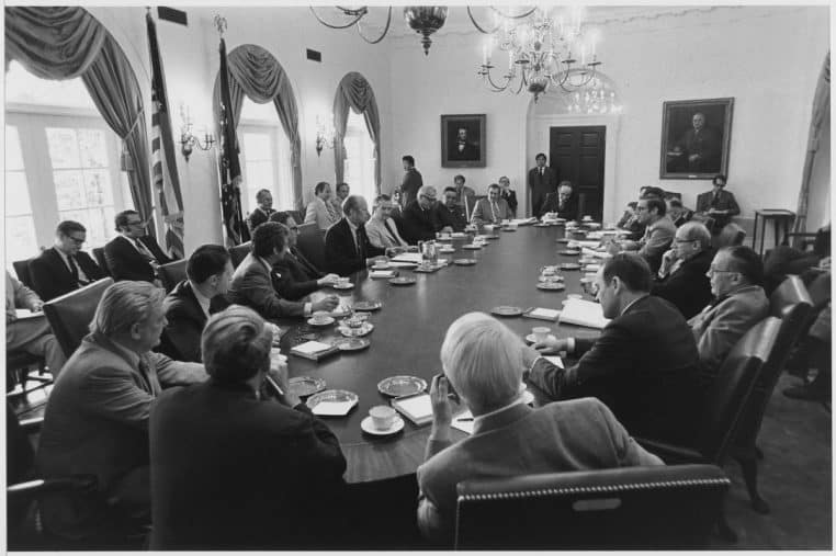 Grande table de réunion entourée de décideurs ; séance de travail officielle dans une salle gouvernementale.