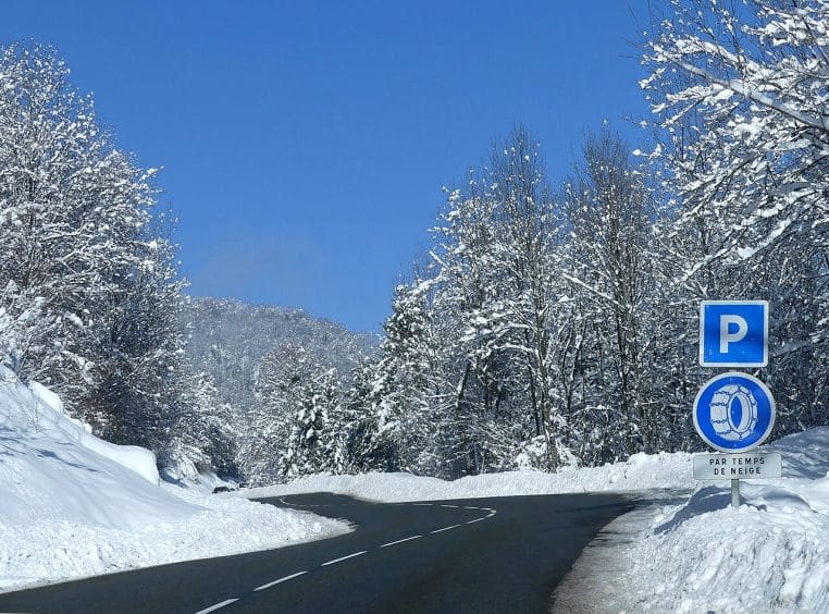 Route de Savoie dégagée avec panneau indiquant une zone pour monter les chaînes à neige avant d’aborder un secteur exposé.