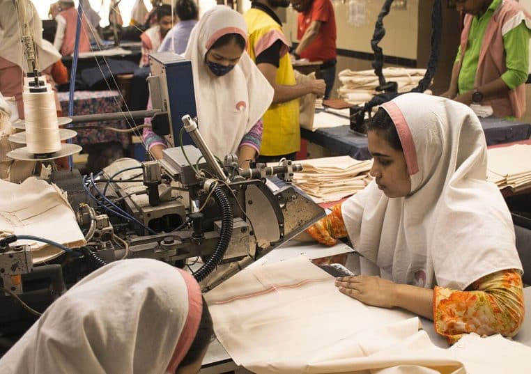 Employées concentrées devant postes de couture et machines, au cœur d’un atelier de confection bangladais.