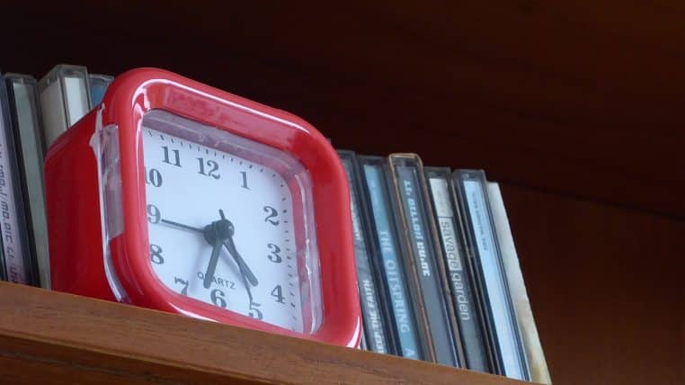 Réveil rouge posé sur une étagère, gros plan sur le cadran à aiguilles, photo nette illustrant le passage à l’heure d’hiver.
