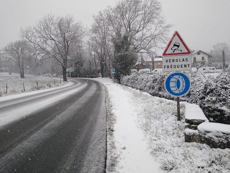 Route enneigée en Haute-Savoie avec panneaux « chaussée glissante », « verglas fréquent » et obligation de chaînes à proximité d’un village.