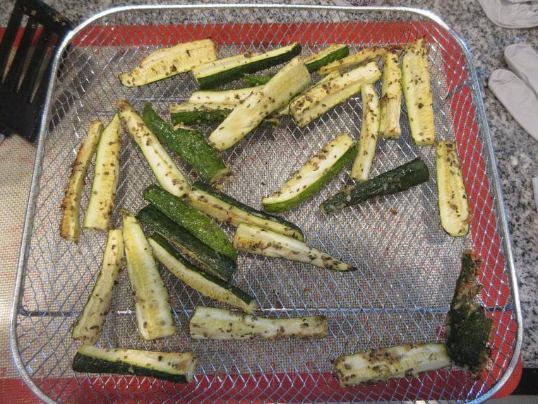Rondelles de courgette assaisonnées d’herbes dans le panier d’une friteuse à air.