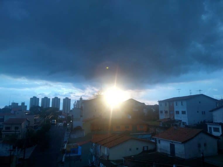 Soleil bas sous un nuage d’orage au-dessus de Taboão da Serra ; silhouettes d’immeubles et toits serrés en avant-plan.