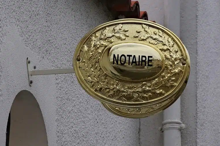 Gros plan horizontal d’un panonceau de notaire à Soyaux, révèle l’emblème doré caractéristique des études notariales.