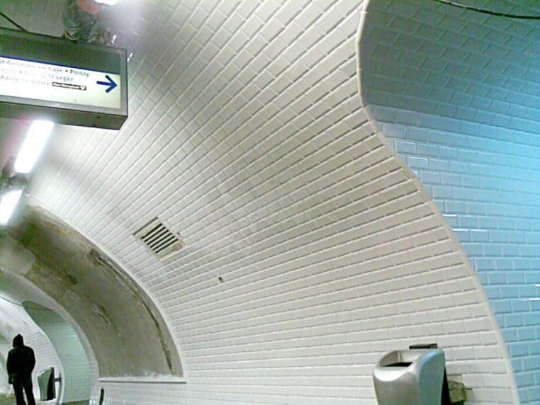 Couloir carrelé aux murs blancs et encadrements céramique, vue horizontale nette des joints et reflets lumineux.