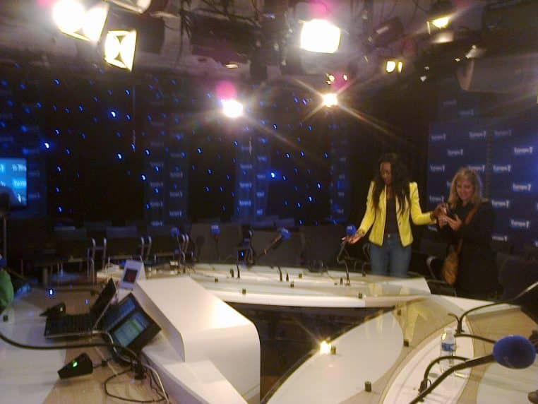 Plateau Europe 1 avec tables, micros bleus et éclairages de studio, arrière-plan aux couleurs de la station, capté pendant une visite.