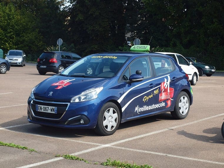 Voiture d’auto-école avec panneau sur le toit, stationnée en ville à Suippes.