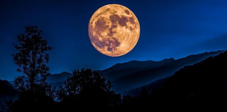 Super Lune se levant au-dessus de sommets himalayens, disque très large et ciel sombre bleu nuit, paysage horizontal net et contrasté