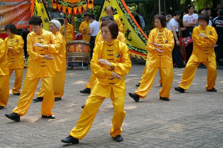 Groupe d’adultes pratiquant le tai-chi en extérieur à Kowloon Park, Hong Kong, séance collective matinale en tenue uniforme, vue large et horizontale.