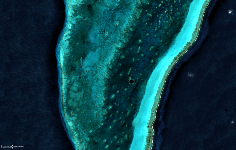 Vue aérienne du Great Blue Hole au Belize, vaste cercle sombre entouré d’un lagon turquoise, révélant le contraste marqué entre faible et grande profondeur.