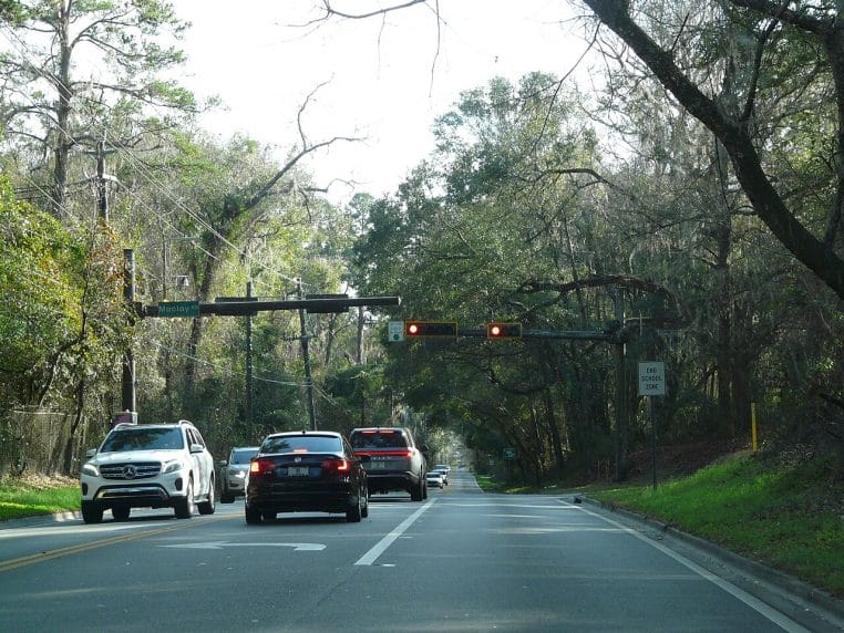 Feu tricolore au rouge au-dessus d’un carrefour urbain, voitures à l’arrêt sur plusieurs voies, vue frontale nette.
