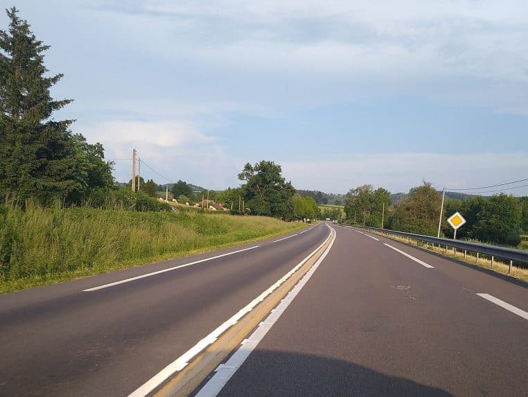 Route nationale avec triple ligne continue au centre, rase campagne en été