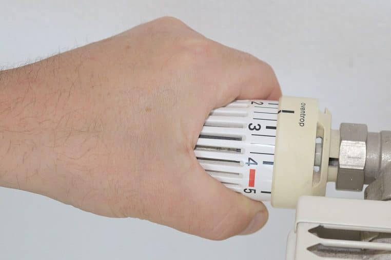 Main tournant une tête thermostatique de radiateur pour ajuster la chaleur pièce par pièce sans surconsommer.