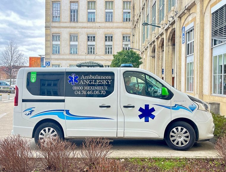 Ambulance blanche stationnée devant l’hôpital de la Croix-Rousse, façade moderne et signalétique hospitalière visibles en arrière-plan.