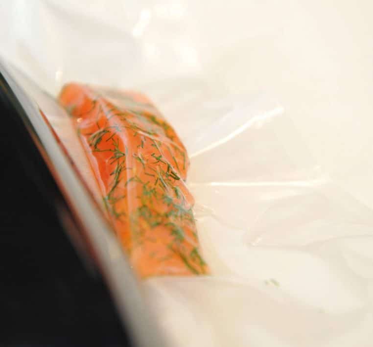 Gros plan d’un filet de saumon recouvert d’herbes, conditionné dans un sachet plastique mis sous vide.