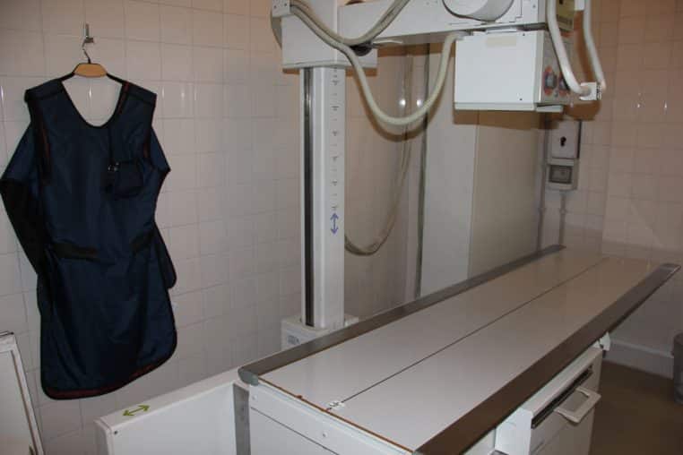 Salle de radiologie vétérinaire avec table mobile et tablier plombé suspendu contre un mur carrelé.