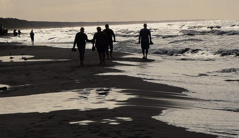 Deux personnes marchent au bord de la mer Baltique sur une vaste plage, horizon dégagé et lumière douce en fin de journée.