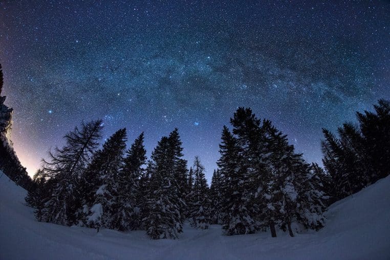 Voie lactée hivernale au-dessus d’une forêt enneigée, ciel clair et arc stellaire visibles, cadrage large en format horizontal.
