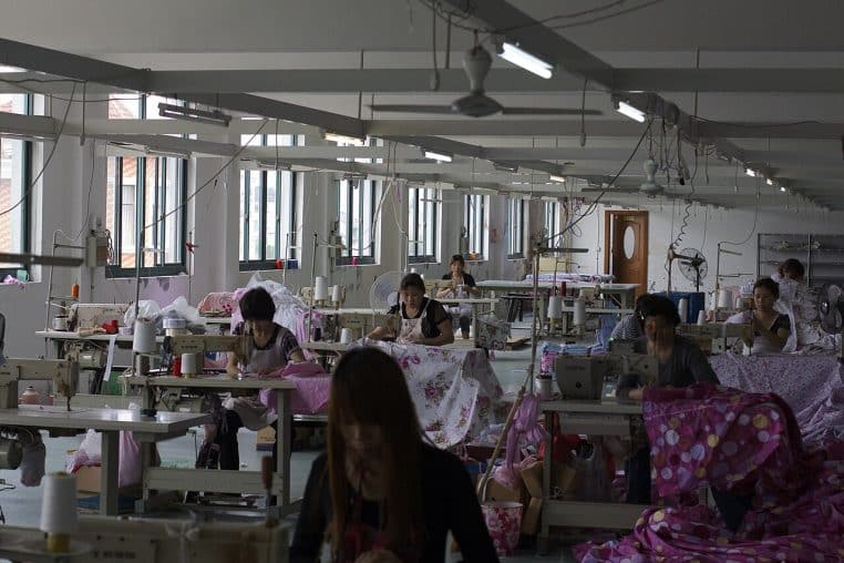 Ouvrières chinoises alignées sur une chaîne de production textile dans une usine de soie, entre bobines et machines industrielles.