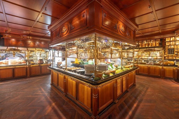 Vue grand angle des buffets d’entrées aux Grands Buffets de Narbonne, vitrines en bois et étals garnis sous lumières chaudes, salle vide.