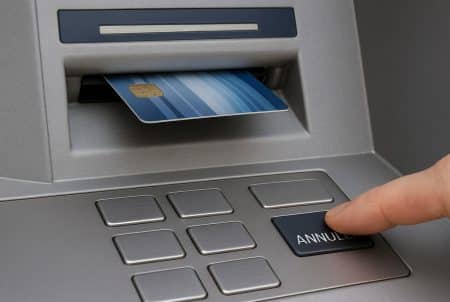 Gros plan d’un distributeur : carte coincée dans la fente tandis qu’un doigt appuie sur la touche « Annuler » pour la récupérer.