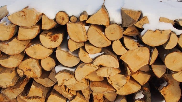 Tas de bois empilé sous la neige près d’une maison de campagne