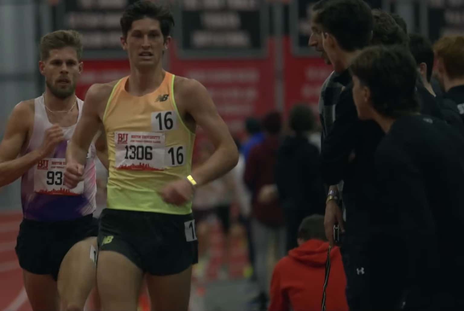 Coureur de fond en débardeur jaune fluo au premier plan, regard concentré, en salle, suivi par un concurrent sur piste indoor.