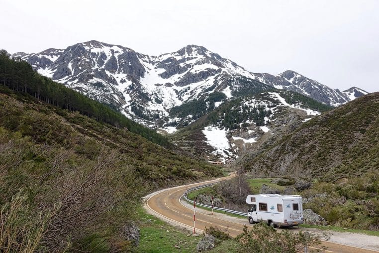 Camping-car roulant sur une route de montagne, reliefs au fond.