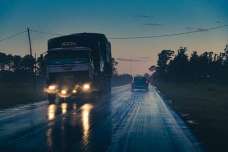 Camion roulant de nuit sur autoroute, phares et ruban lumineux au loin.