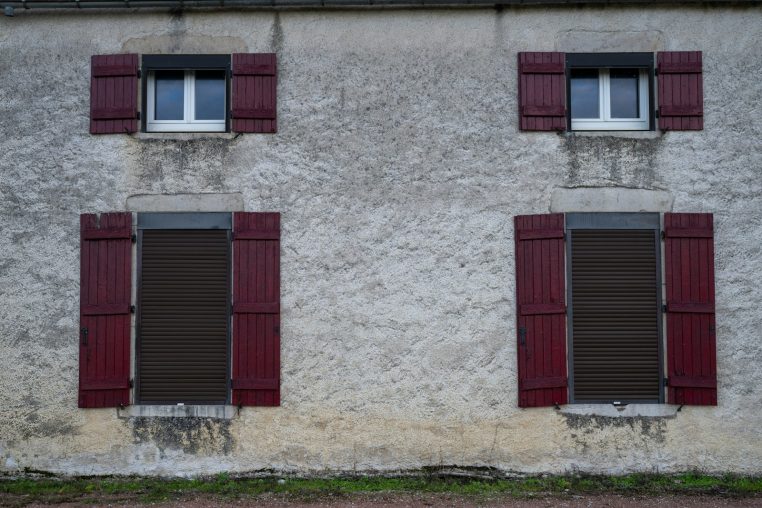 Four windows with red shutters on a textured wall