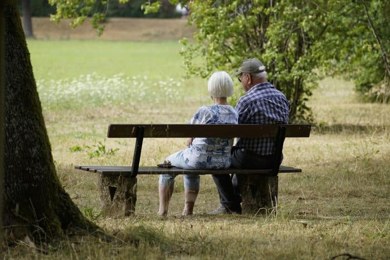 Couple de retraités assis sur un banc dans un parc, regardant devant eux, scène paisible en extérieur au format horizontal.