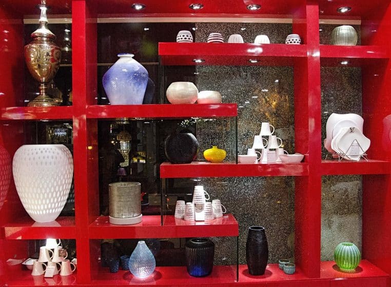 Showroom design avec étagères rouges éclairées, vases et vaisselle alignés, ambiance magasin moderne et soignée en plan large.