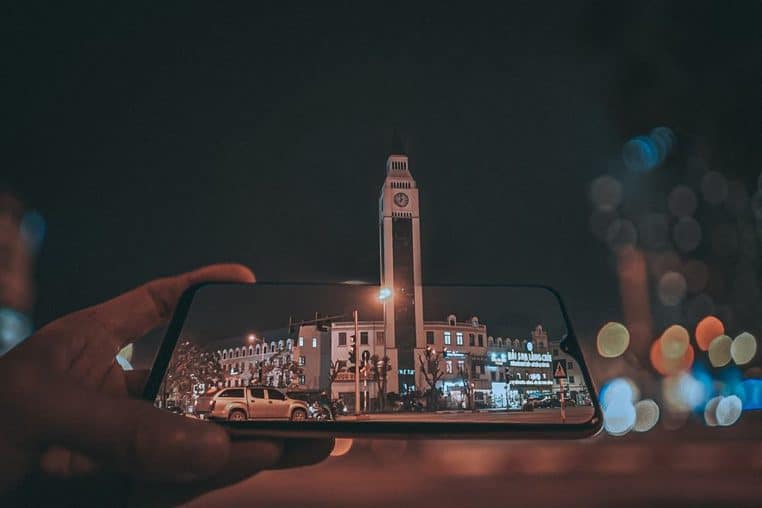 Main tenant un smartphone au cœur d’une ville de nuit