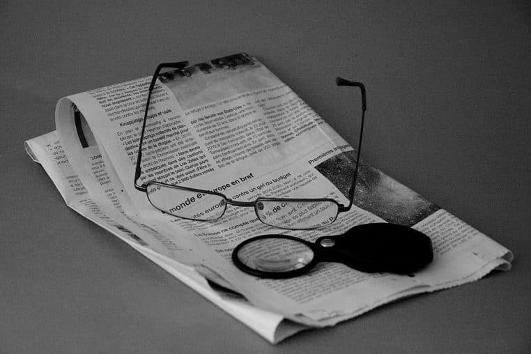 Lunettes posées sur un journal plié, gros plan horizontal évoquant la lecture des informations financières.