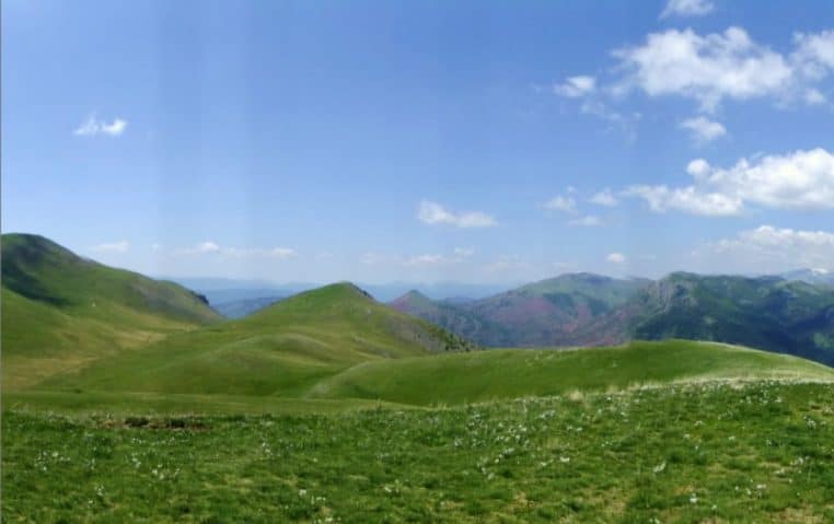 Large panorama des reliefs autour de Roubion, crêtes étirées et vallons ouverts sous un ciel clair aux teintes d’hiver.